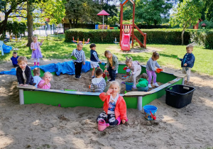 Dzieci wspólnie bawią się w piaskownicy, przesypując piasek do foremek i wiaderek.