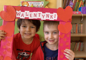 dzieci pozują do zdjęcia trzymając w dłoni czerwoną ramkę z napisem Walentynki
