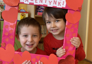 dzieci pozują do zdjęcia trzymając w dłoni czerwoną ramkę z napisem Walentynki