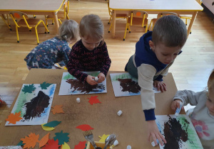 przedszkolaki przyklejają kolorowe liście na kartce papieru