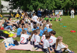 zawodnicy siedzą na kocach oglądają pokaz karate