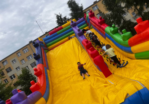 Dzieci z szerokimi uśmiechami zjeżdżają na dmuchanym zamku.