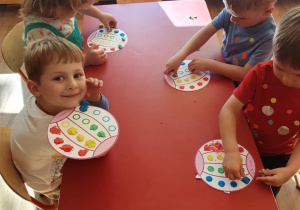 przedszkolaki naklejają plastelinę na kartkę papieru