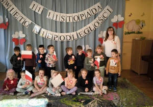 Wspólne zdjęcie grupy III po akademii – pozują razem. W tle widać biało-czerwone dekoracje, a dzieci z dumą prezentują swoje flagi i kotyliony.