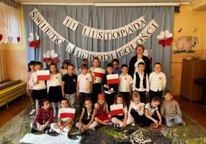 Wspólne zdjęcie grupy V po akademii – pozują razem. W tle widać biało-czerwone dekoracje, a dzieci z dumą prezentują swoje flagi i kotyliony.