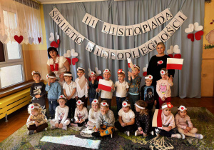 Wspólne zdjęcie grupy II po akademii – pozują razem. W tle widać biało-czerwone dekoracje, a dzieci z dumą prezentują swoje flagi i kotyliony.