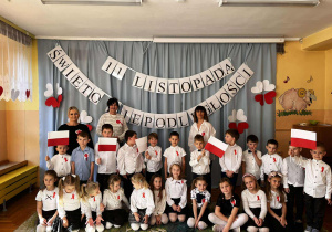 Nauczyciele z dziećmi – wspólne zdjęcie wychowawców z grupą przedszkolną. Wszyscy ubrani w odświętne barwy, dumni z pięknych występów swoich podopiecznych.