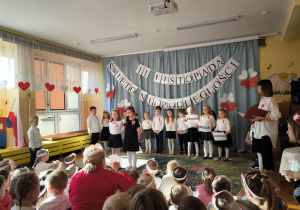 Wspólne zdjęcie po akademii – dzieci z grupy VI pozują razem. W tle widać biało-czerwone dekoracje, a dzieci z dumą prezentują swoje flagi i kotyliony.