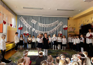 Na następnym zdjęciu widzimy dziewczynki w białych bluzkach i czarnych spódniczkach, które recytują wiersze o Polsce.