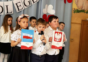 występ najstarszej grupy – dzieci prezentują inscenizację o drodze Polski do niepodległości. W tle widnieje dekoracja w barwach narodowych: biało-czerwona flaga, godło oraz napisy „11 listopada – Święto Niepodległości”.