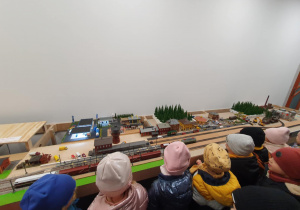 Model kolejki i pociągów ustawiony na osobnym stanowisku – dzieci z dużym zainteresowaniem przyglądają się wagonikom.