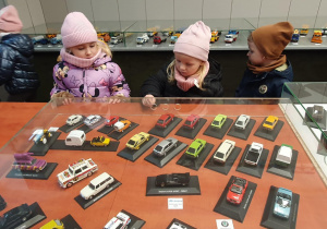 Dzieci pozują uśmiechnięte przy stole pełnym wyjątkowych modeli – pamiątkowe zdjęcie z wystawy.