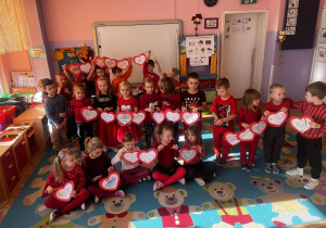 Grupa dzieci prezentuje gotowe prace – trzymają własnoręcznie wykonane czerwone serca. Na ich twarzach widać dumę, radość oraz poczucie wspólnego celu.