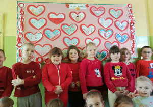 Dzieci stoją przed tablicą ozdobioną czerwonymi sercami – symbolem życzliwości, miłości i bezpieczeństwa.