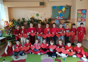 Dzieci stoją przed tablicą ozdobioną czerwonymi sercami – symbolem życzliwości, miłości i bezpieczeństwa.