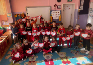 Dzieci stoją przed tablicą ozdobioną czerwonymi sercami – symbolem życzliwości, miłości i bezpieczeństwa.