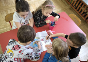przedszkolaki siedzą przy stoliku, kolorują misia
