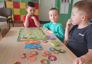 Na zdjęciu widać dzieci siedzące przy stoliku, które wspólnie grają w grę edukacyjną „Odkryj siebie i poznaj swoje emocje”.