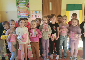 Na zdjęciu widać grupę starszaków z przedszkola. Dziewczynki trzymają w rękach upominki otrzymane od chłopców z grupy. Dzieci są uśmiechnięte i widać, że są zadowolone z otrzymanych prezentów.