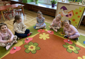 Na zdjęciu widać grupę dzieci siedzących na dywanie po turecku. Przed nimi poukładane są przygotowane upominki. Dzieci patrzą w stronę aparatu, pokazując zainteresowanie i radość z otrzymanych prezentów.