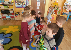 Dziewczynki z radością odbierają prezenty od chłopców i dziękują im za nie. Dzieci uśmiechają się, a zdjęcie pokazuje miły i pełen ciepła moment w przedszkolu.