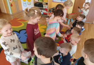 Dziewczynki z radością odbierają prezenty od chłopców i dziękują im za nie. Dzieci uśmiechają się, a zdjęcie pokazuje miły i pełen ciepła moment w przedszkolu.