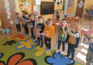 Na zdjęciu chłopcy stoją w grupie, trzymając w rękach przygotowane upominki dla dziewczynek. Uśmiechają się i patrzą w stronę aparatu.