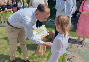 Na zdjęciu widoczne jest jury konkursu w trakcie gratulowania uczestnikom. Dzieci otrzymują dyplomy oraz nagrody rzeczowe, a pozostali uczestnicy obserwują wydarzenie z zainteresowaniem i dumą.