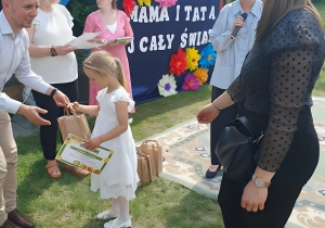 Fotografia przedstawia moment wręczania nagród podczas konkursu. Dzieci ustawione są obok organizatorów, którzy przekazują dyplomy i drobne upominki. Uroczystość odbywa się w radosnej atmosferze.