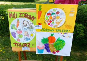 Na zdjęciu widoczne są prace plastyczne wykonane przez dzieci i ich rodziny, przedstawiające kolorowe talerze z podziałem na zdrowe produkty spożywcze. Wśród nich znajdują się owoce, warzywa, produkty zbożowe oraz nabiał. Prace są wykonane różnymi technikami – rysunek, wyklejanka oraz kolaż.
