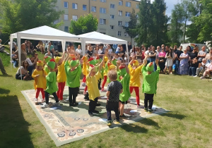 a zdjęciu widoczny jest moment występu dzieci na scenie festynu rodzinnego. Przedszkolaki tańczą w grupie, a ich występ spotyka się z zainteresowaniem i życzliwym odbiorem ze strony publiczności.