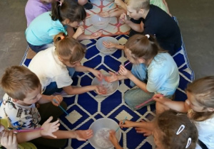 Podczas zajęć sensorycznych dzieci uczestniczą w zabawie z pianą. Kucając wokół maty, obserwują proces jej powstawania i aktywnie biorą udział w eksperymentach. Wspólna aktywność dostarcza wielu wrażeń i zachęca do odkrywania świata poprzez zmysły.