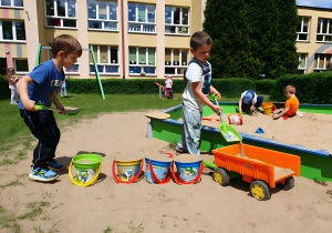Na zdjęciu widoczne są przedszkolaki korzystające z ogrodu dydaktycznego. Dzieci aktywnie uczestniczą w zabawie piaskiem, tworząc różnorodne formy i konstrukcje, co dostarcza im wiele radości i satysfakcji.