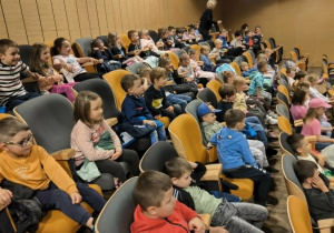Na zdjęciu dzieci zgromadzone na widowni obserwują przedstawienie teatralne. Uczestnicy wyjścia kulturalnego aktywnie odbierają prezentowaną historię i emocje bohaterów.