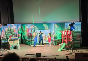 Dzieci z przedszkola oglądają przedstawienie teatralne „Karolcia” w Centrum Integracji Ratusz. Na scenie aktorzy prezentują spektakl w kolorowej scenerii, a młodzi widzowie z zainteresowaniem śledzą przebieg wydarzeń.