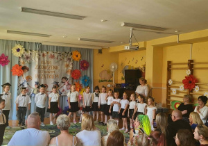 Dzieci prezentują część artystyczną przygotowaną na zakończenie edukacji przedszkolnej. Na tle dekoracji z motywem absolwentów przedszkolaki recytują wiersze i śpiewają piosenki. Wydarzenie odbywa się w obecności rodziców oraz pracowników przedszkola.
