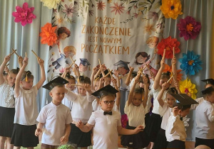 Dzieci prezentują część artystyczną przygotowaną na zakończenie edukacji przedszkolnej. Na tle dekoracji z motywem absolwentów przedszkolaki recytują wiersze i śpiewają piosenki. Wydarzenie odbywa się w obecności rodziców oraz pracowników przedszkola.