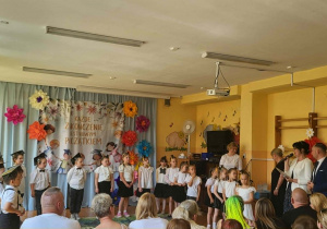 Dzieci prezentują część artystyczną przygotowaną na zakończenie edukacji przedszkolnej. Na tle dekoracji z motywem absolwentów przedszkolaki recytują wiersze i śpiewają piosenki. Wydarzenie odbywa się w obecności rodziców oraz pracowników przedszkola.