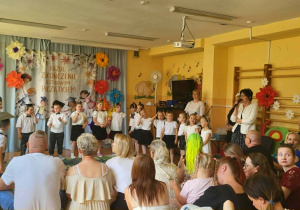 Pani dyrektor kieruje do absolwentów przedszkola serdeczne życzenia sukcesów w szkole oraz podziękowania za wspólnie spędzony czas. W tle widoczne są kolorowe dekoracje podkreślające wyjątkowy charakter uroczystości.