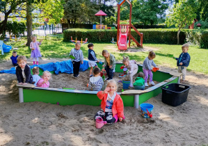 Dzieci wspólnie bawią się w piaskownicy, przesypując piasek do foremek i wiaderek.