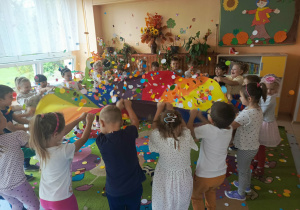 Dzieci uczestniczą w zabawie ruchowej z chustą animacyjną, obserwując unoszące się nad nią kropki