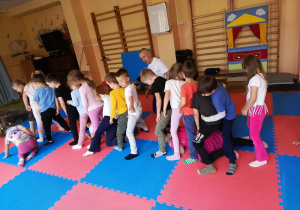 Przedszkolaki wykonują różnorodne ćwiczenia ruchowe na matach pod okiem instruktora judo