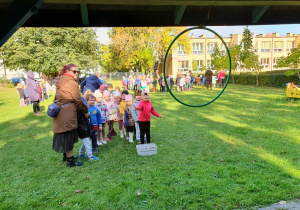 Dzieci stoją ustawione w rzędzie i czekają na swoją kolej, aby wykonać przygotowane zadanie ruchowe. Z zaangażowaniem obserwują przebieg konkurencji i przygotowują się do wspólnej zabawy.