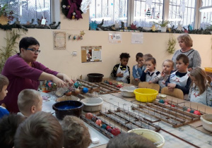 w fabryce bombek, pani dekoratorka pokazuje dzieciom materiały do zdobienia bombek