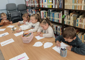 Przedszkolaki siedzą przy stolikach i z zaangażowaniem kolorują jesienne liście. Dzieci dobierają barwy inspirowane jesienną przyrodą, rozwijając kreatywność i sprawność manualną.