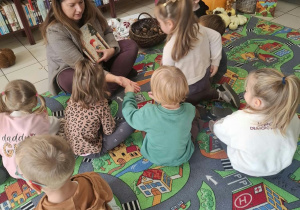 Dzieci siedzą w bibliotece i słuchają jesiennego opowiadania. Przed nimi znajduje się koszyk z darami jesieni, w którym zgromadzono kolorowe liście i inne jesienne skarby.