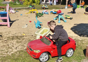 Małe pojazdy, wielka frajda – dzieci korzystają z rekreacyjnych samochodzików i traktorków na placu zabaw, rozwijając koordynację ruchową i czerpiąc radość ze wspólnej aktywności.