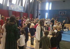 Uczestnicy spotkania stoją w kręgu i biorą udział w zabawie ruchowej, współpracując ze sobą i czerpiąc radość ze wspólnie spędzonego czasu.