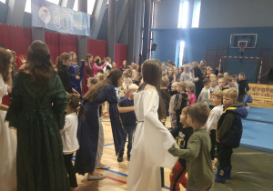Uczestnicy spotkania stoją w kręgu i biorą udział w zabawie ruchowej, współpracując ze sobą i czerpiąc radość ze wspólnie spędzonego czasu.