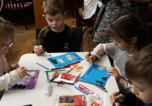 dzieci malują pędzelkami na niebieskich kartkach